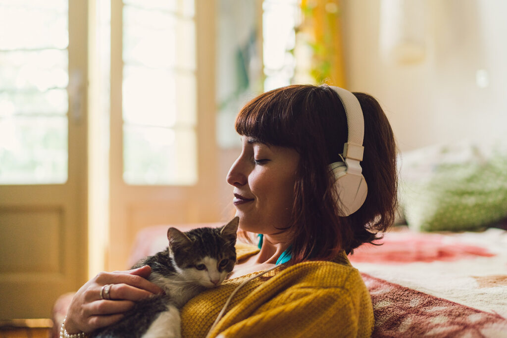 A woman with a cat on her chest listening to music through headphones