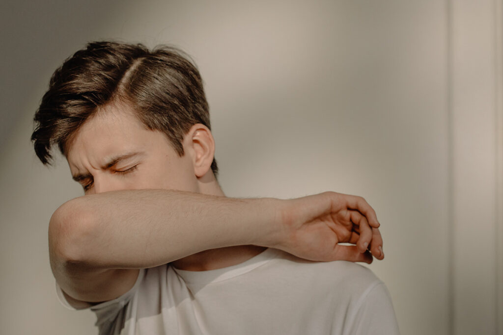 A man sneezing into his elbox