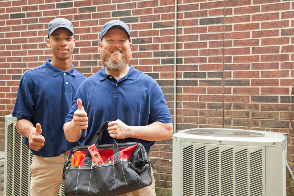 A pair of technicians giving a thumbs up next to an outdoor A/C unit